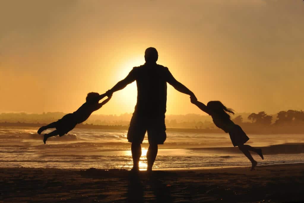 Man on beach at sunset swinging a child from each arm.